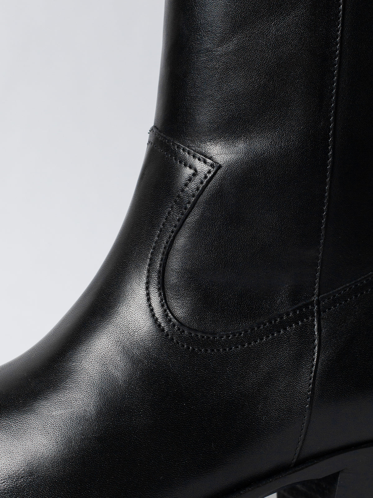 Close-up of a black leather boot with detailed stitching on a light gray background