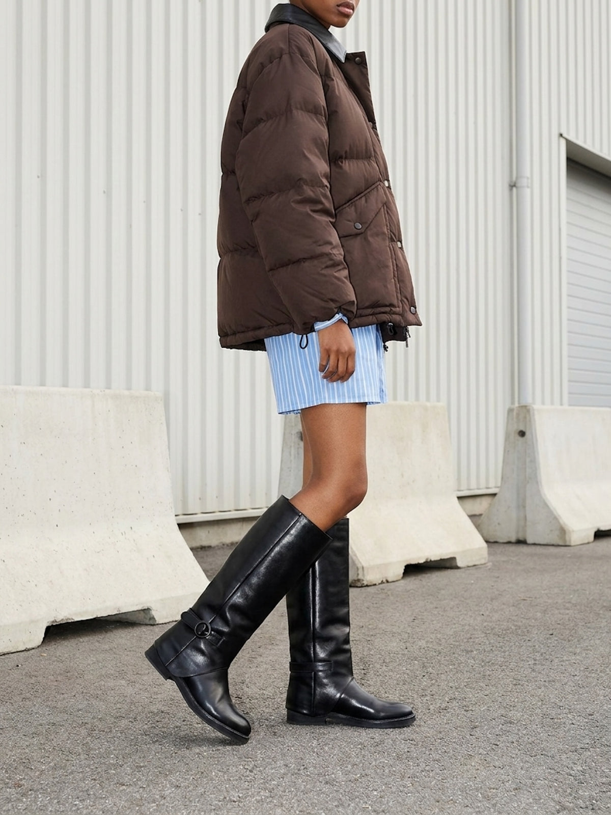 Person wearing a brown puffer jacket and black knee-high boots in an urban setting.