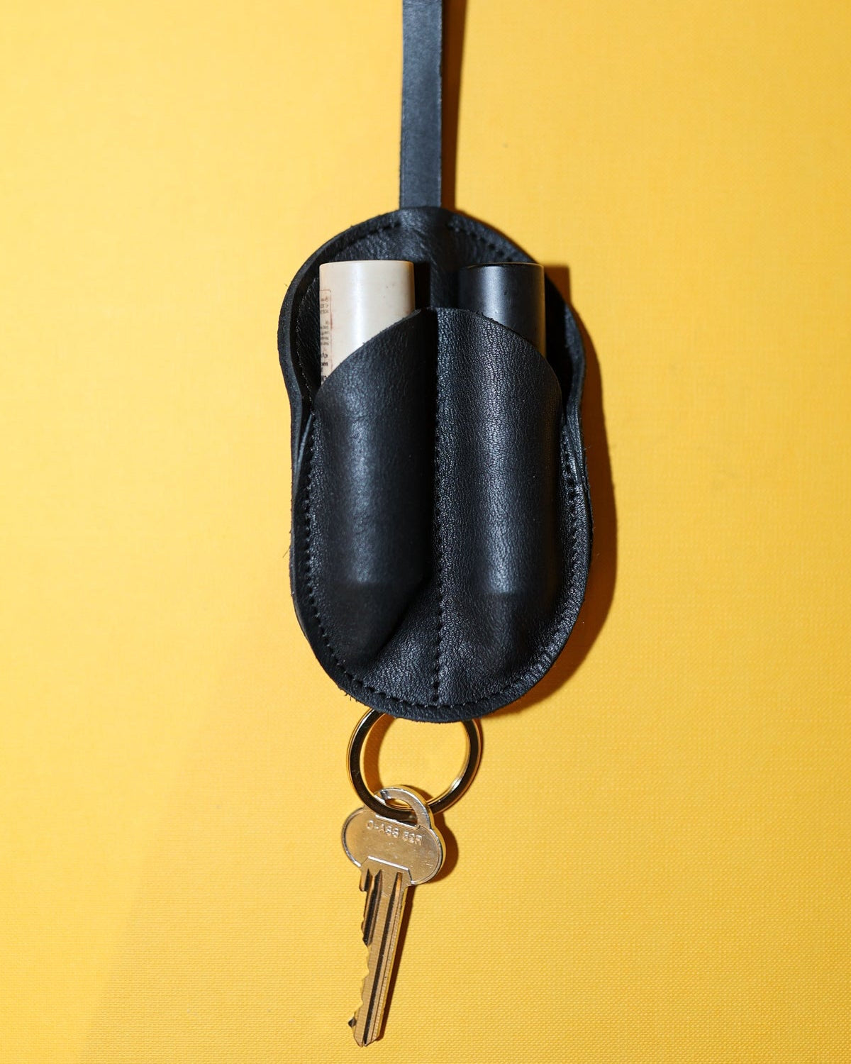 Black leather keychain holder with keys on a yellow background