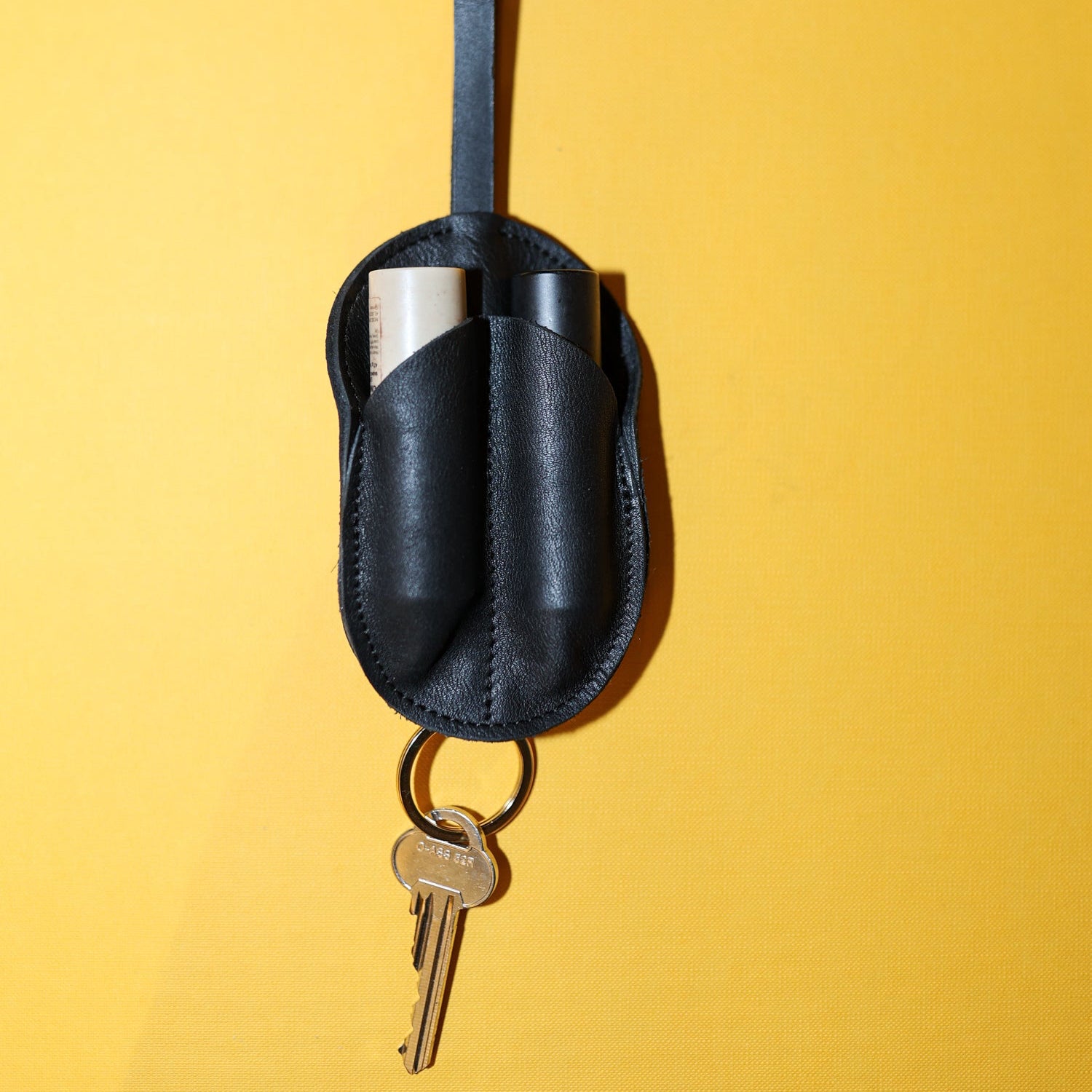 Black leather keychain holder with keys on a yellow background