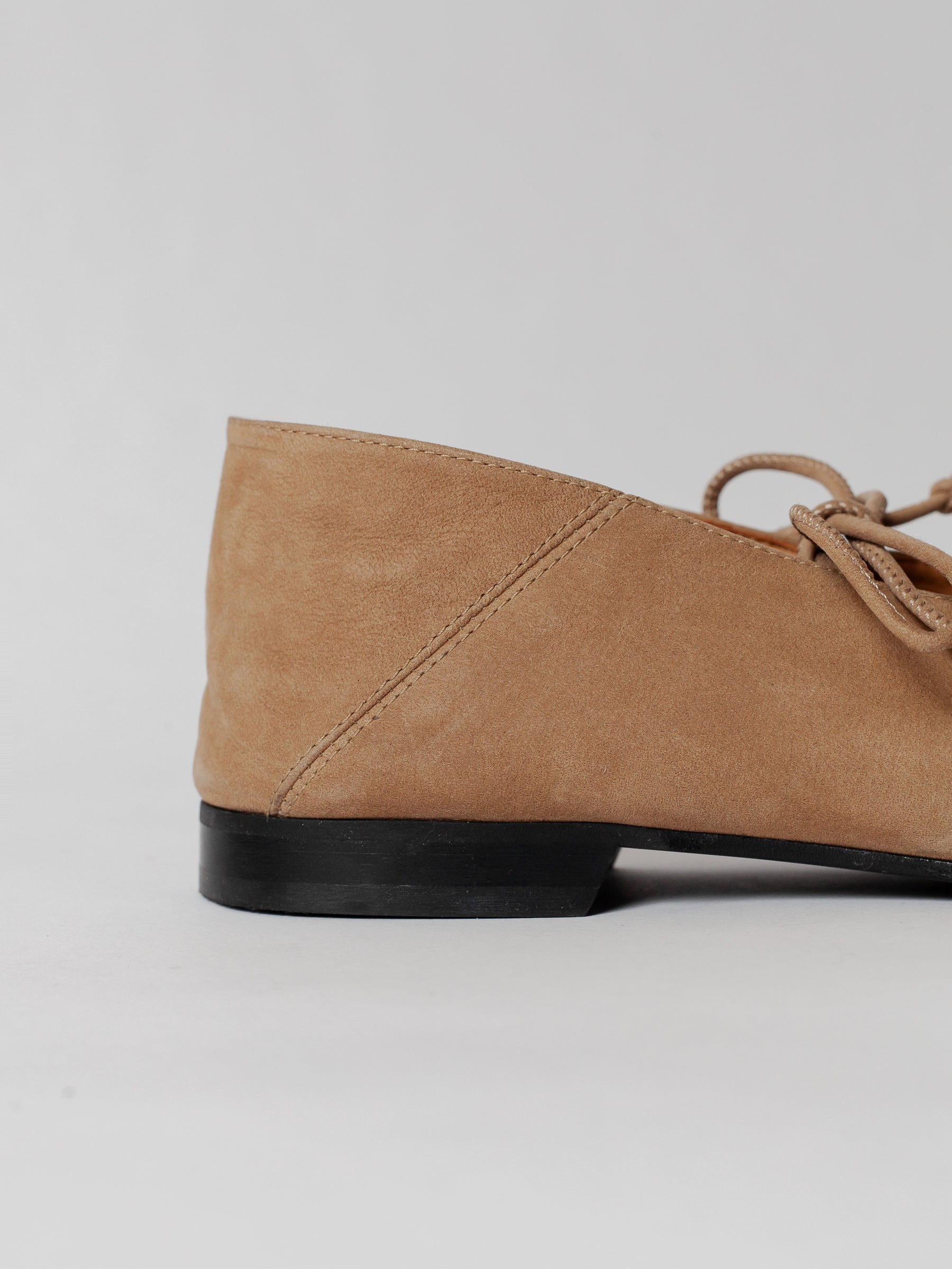 Tan suede shoe with a black sole on a light gray background