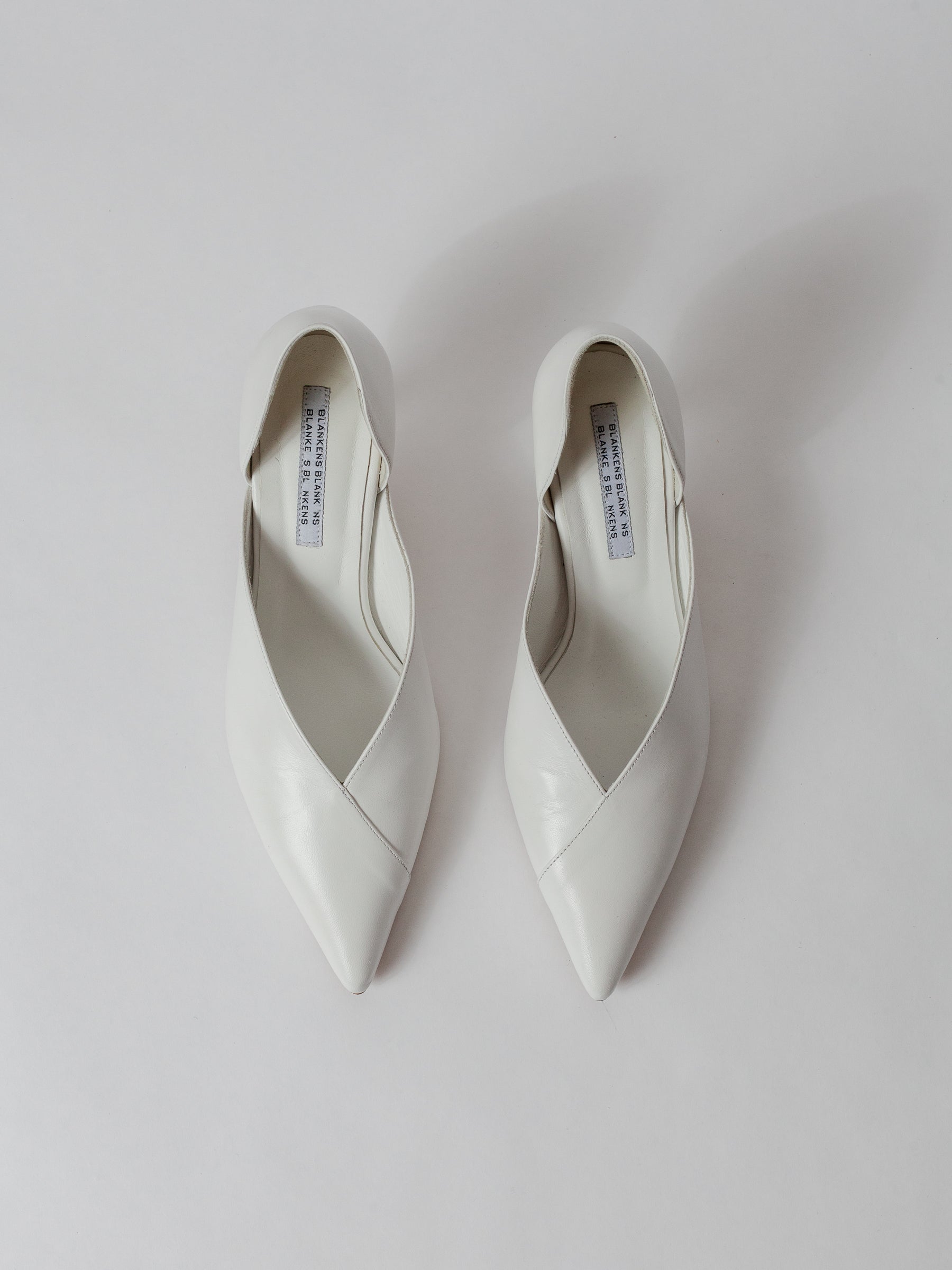 Pair of white pointed-toe shoes on a light gray background