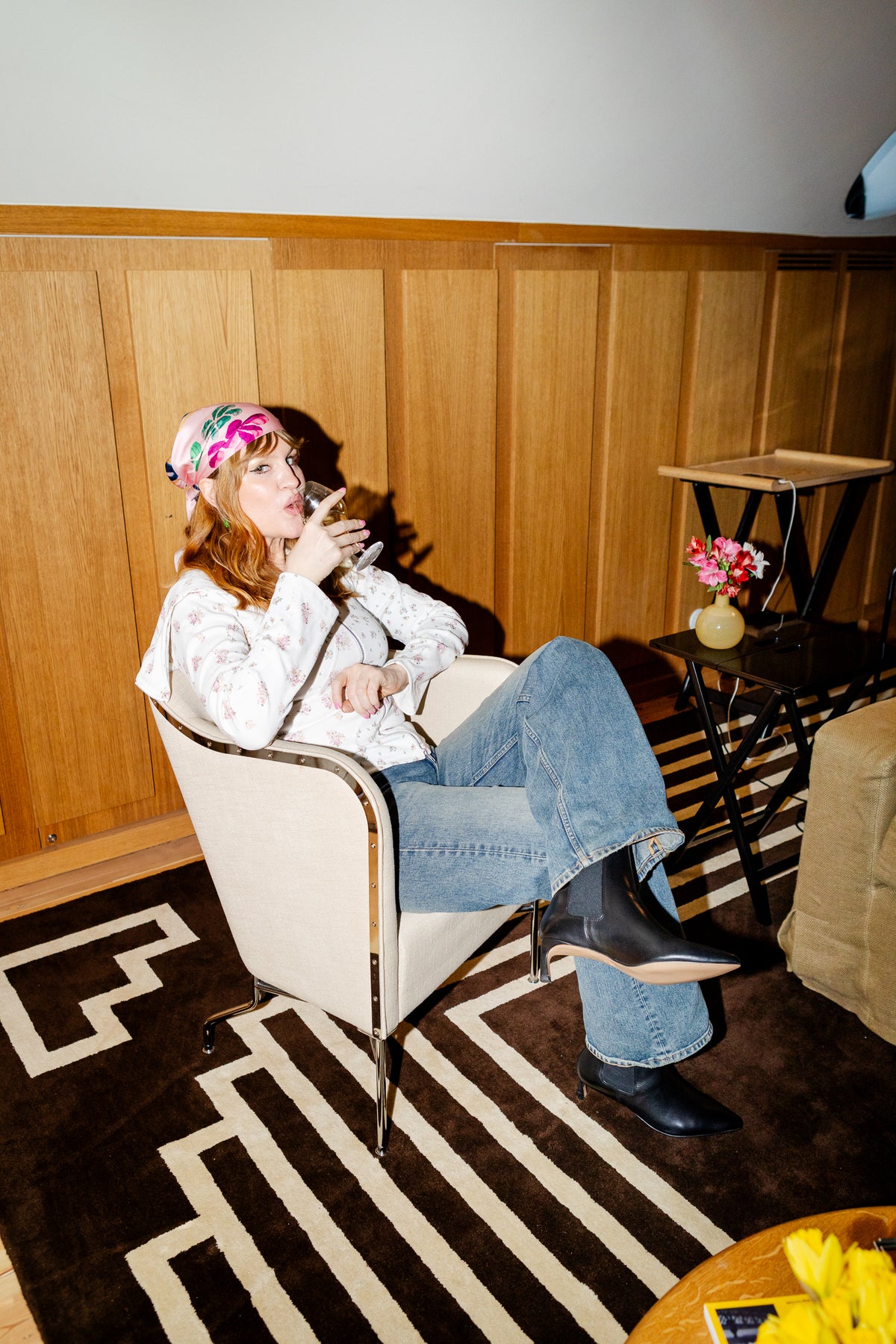 Woman sitting in a chair with a wooden panel wall and rug in the background