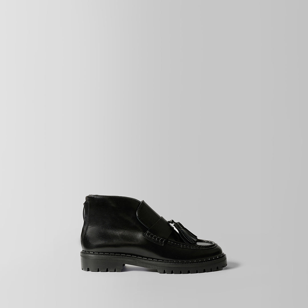 A single black leather ankle boot with a tassel detail on the vamp and a chunky lug sole, photographed from the side against a light gray background.