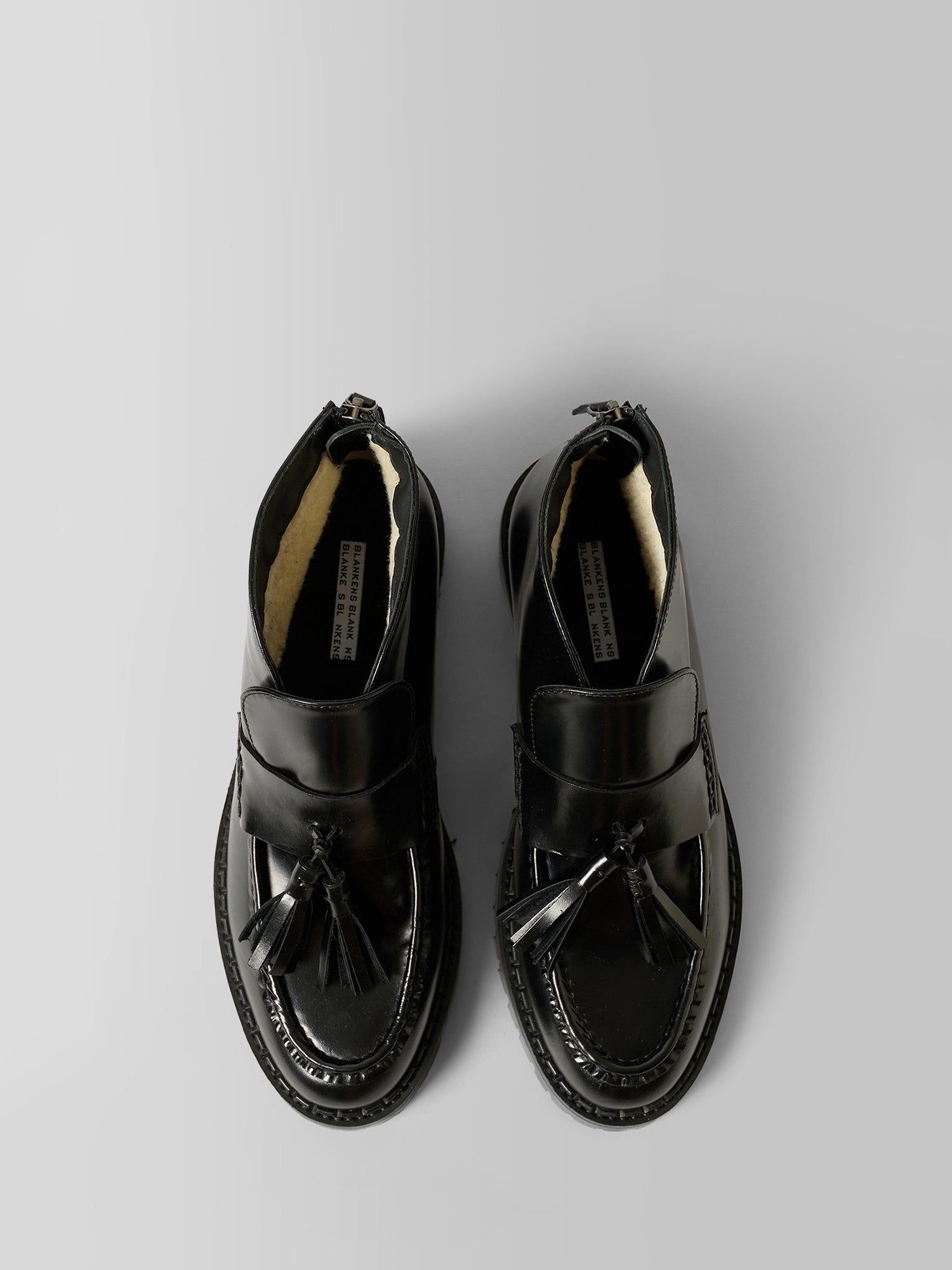 A pair of black leather penny loafers with tassel details, photographed from a top-down perspective on a neutral gray background.