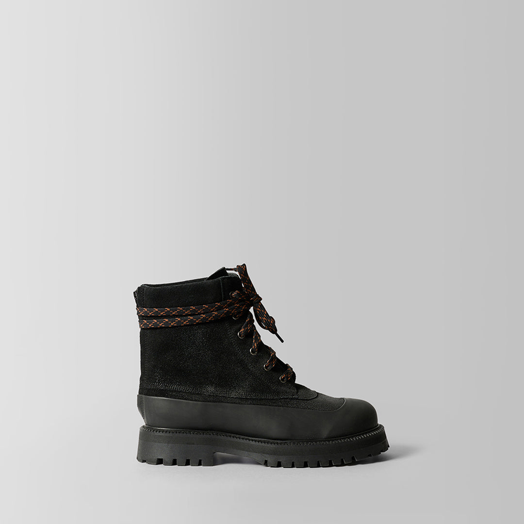 A single black lace-up ankle boot with a thick lug sole, black suede upper, and a brown braided detail around the collar, shown against a light gray background.