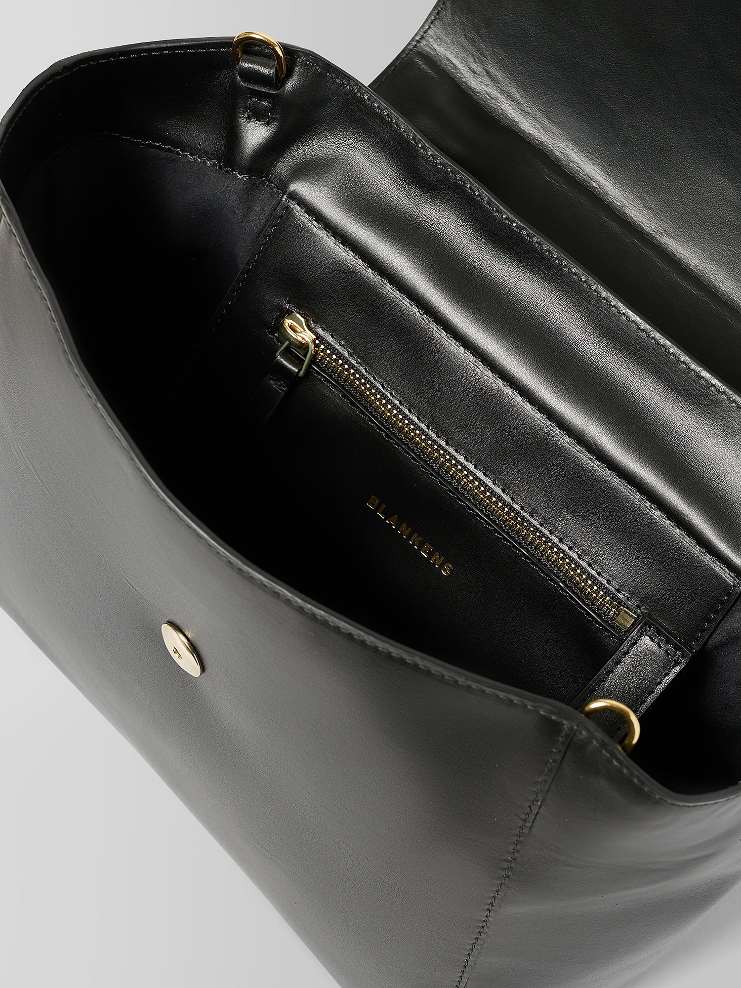 Close-up of a black leather handbag interior showing a zippered pocket with gold-tone hardware and the brand name 'J'ADORE' printed inside.