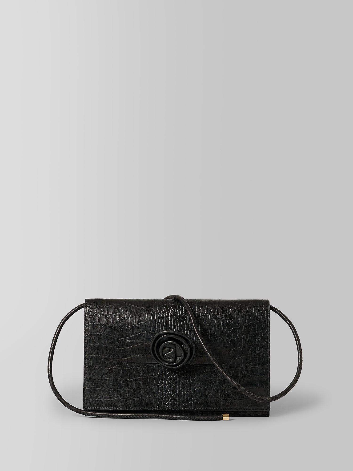 A black crocodile-embossed leather clutch bag with a central rose-shaped clasp and a thin black shoulder strap, shown against a neutral light gray background.