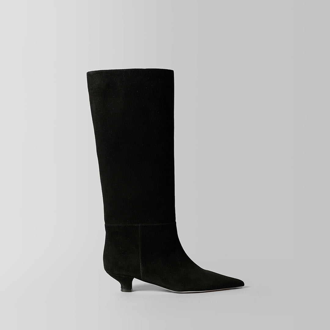 A single black suede knee-high boot with a pointed toe and a low kitten heel, shown in profile against a light gray studio background.
