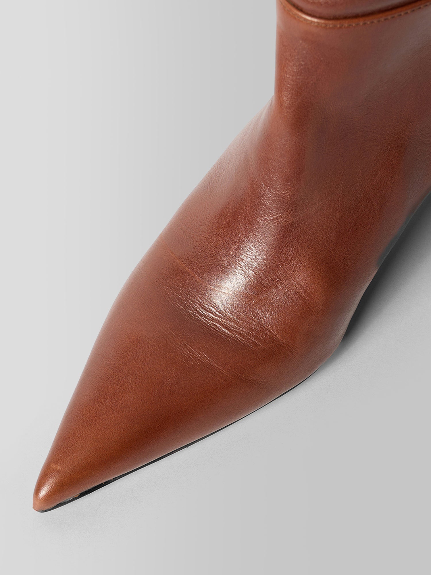 Close-up of a pointed-toe ankle boot in smooth brown leather, showing the toe and side profile against a light gray background.