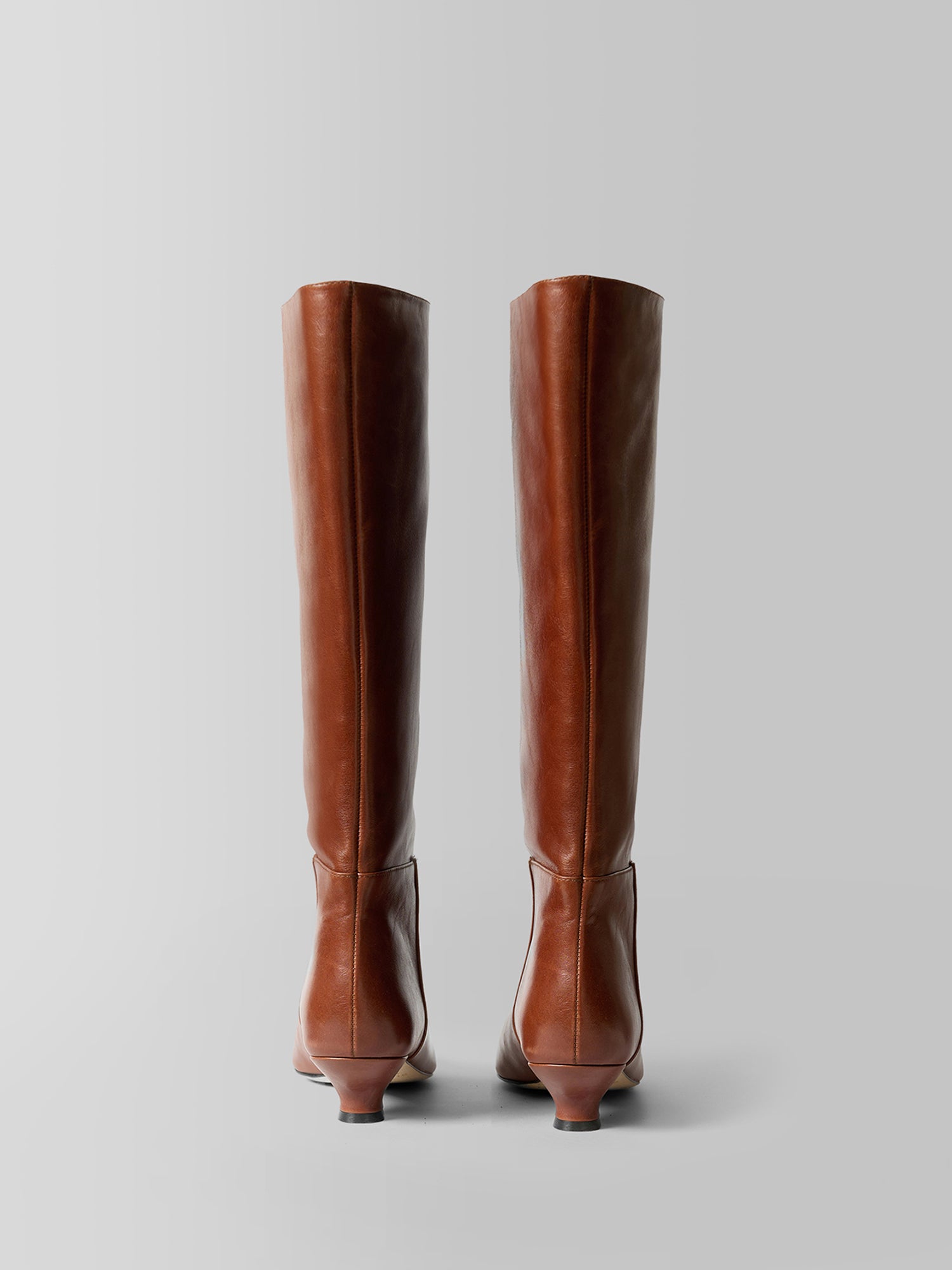 A pair of tall brown leather knee-high boots shown from the back against a neutral light gray background.