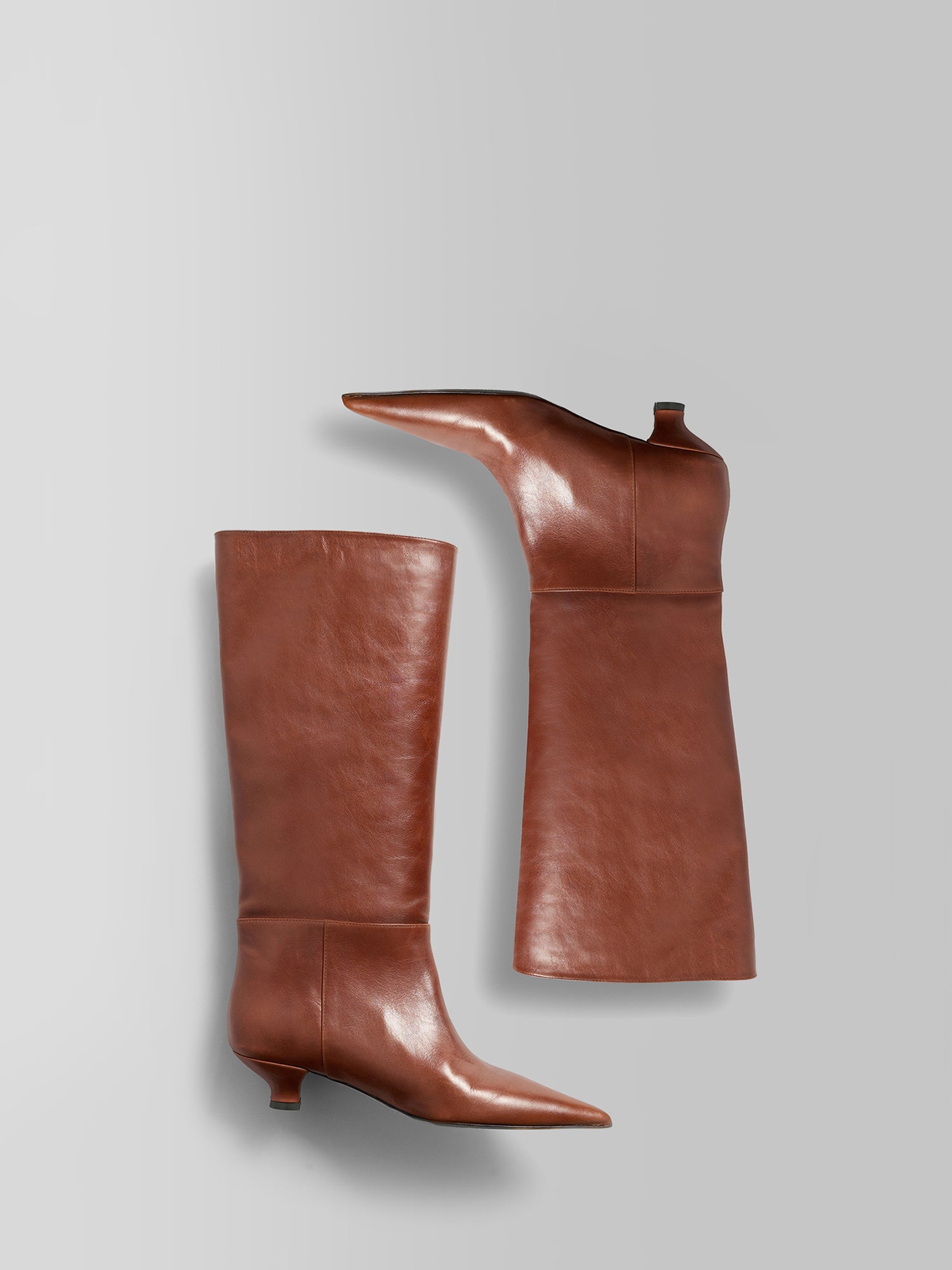 A pair of knee-high brown leather boots with pointed toes and low block heels, displayed on a light gray background.