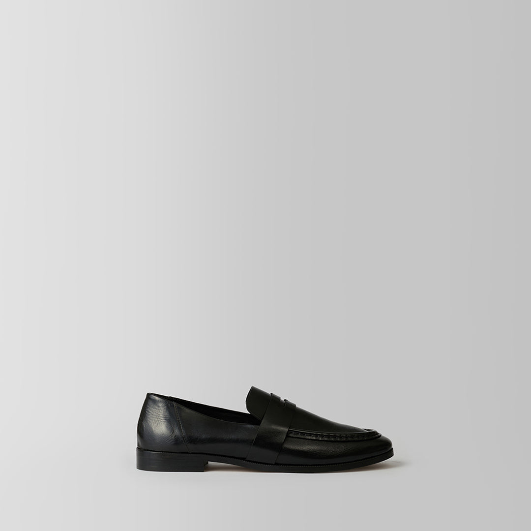 A single black leather penny loafer shown in profile against a light gray studio background.