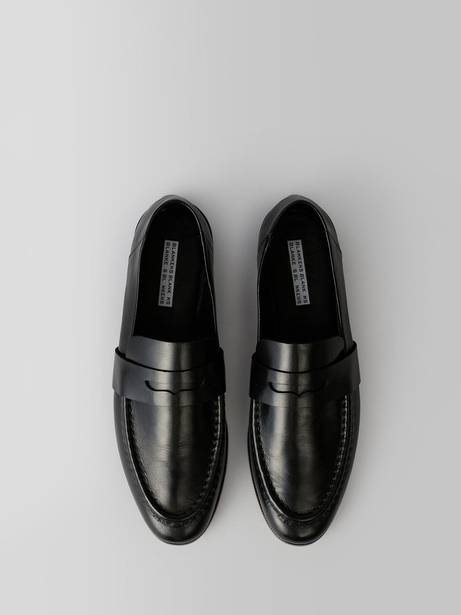 A pair of black leather penny loafers shown from a top-down view on a light gray background.