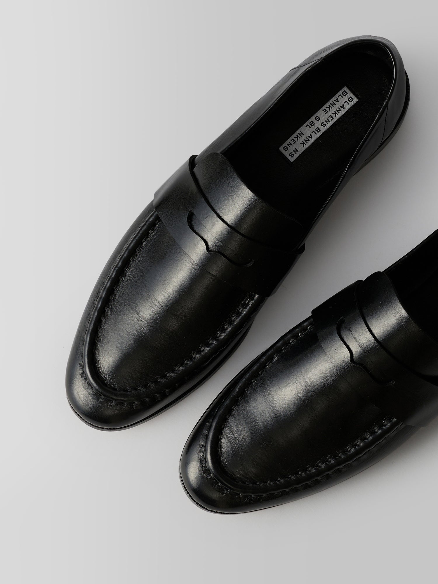 A pair of black leather penny loafers shown from a top-down angle on a light gray background. The brand name 'PLAYING DRESS' is visible on the inner label.