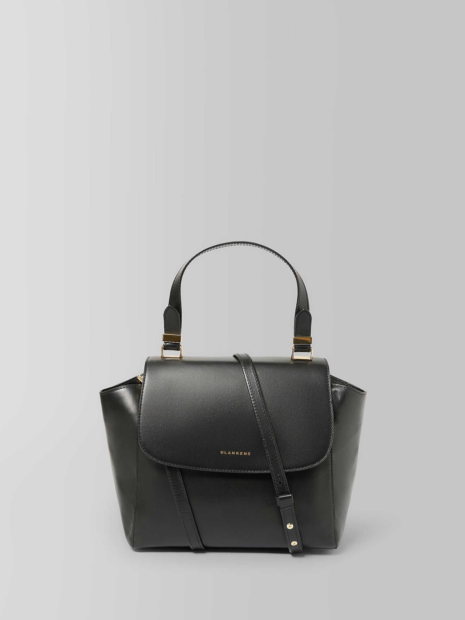 A black leather handbag with a structured top handle, a front flap, and a detachable shoulder strap, photographed against a neutral light gray background.