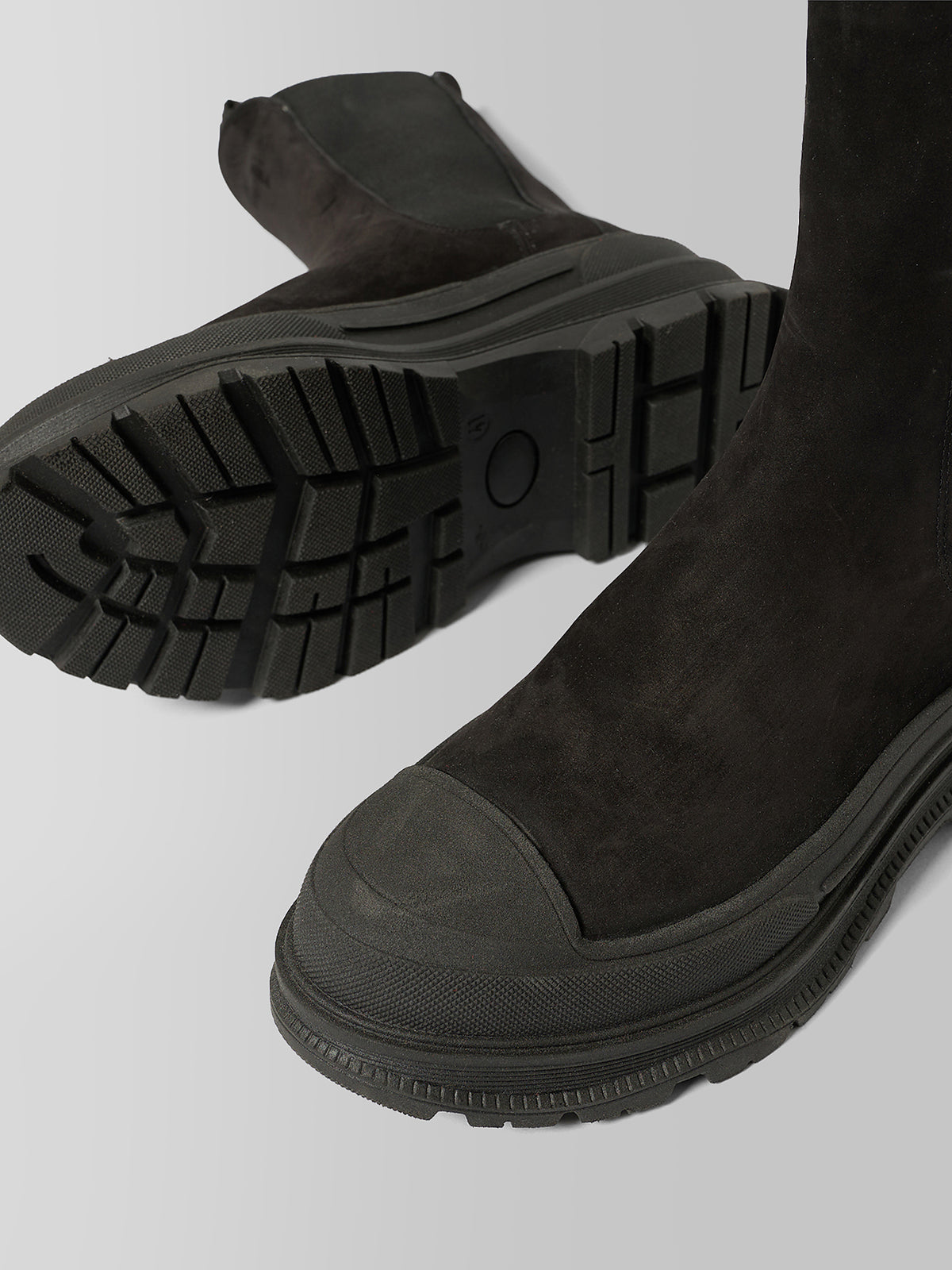 Black suede ankle boots with chunky lug soles, shown from the side and sole detail on a light gray background.