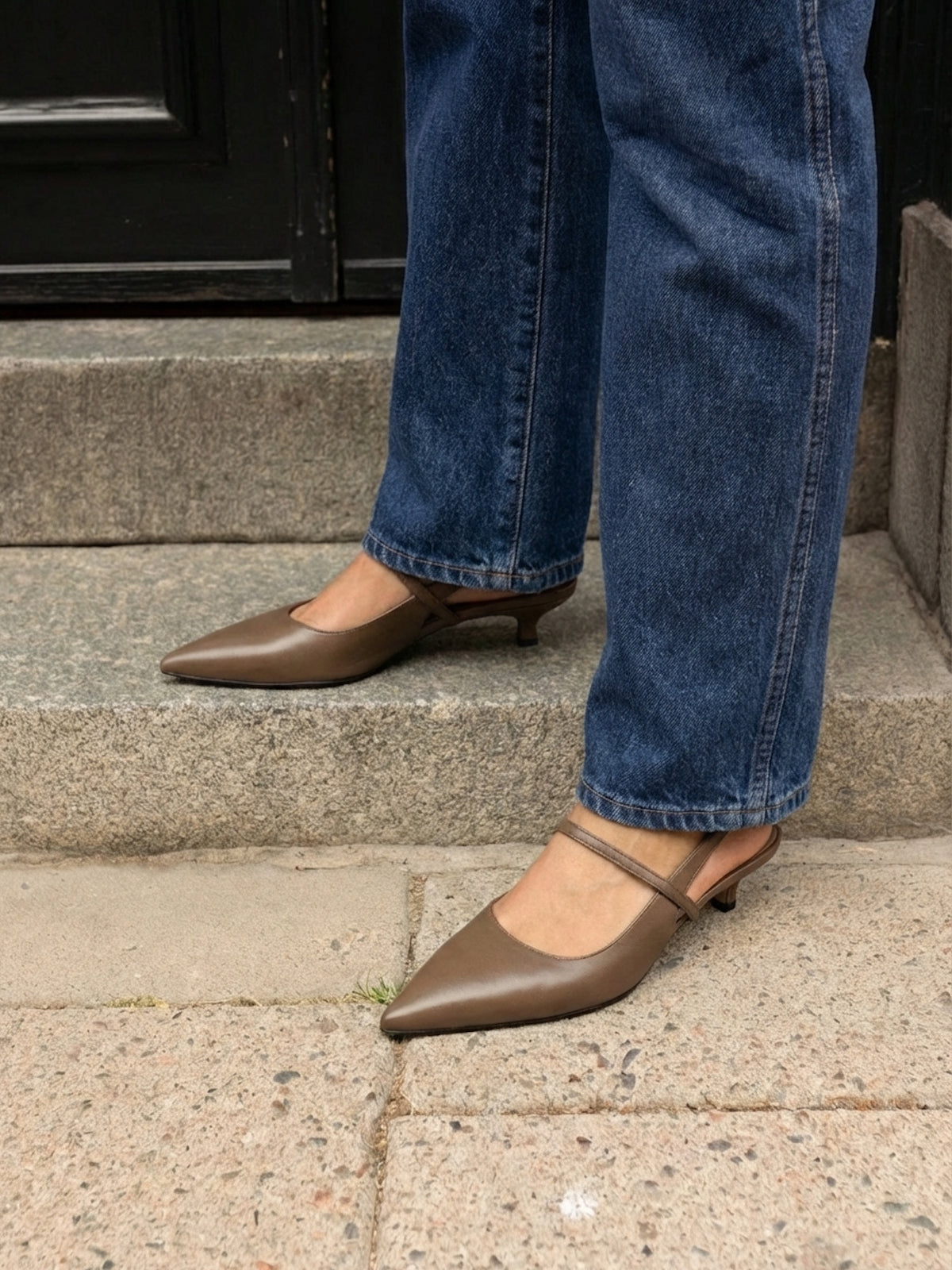 Person wearing brown pointed-toe shoes and blue jeans on a stone step.