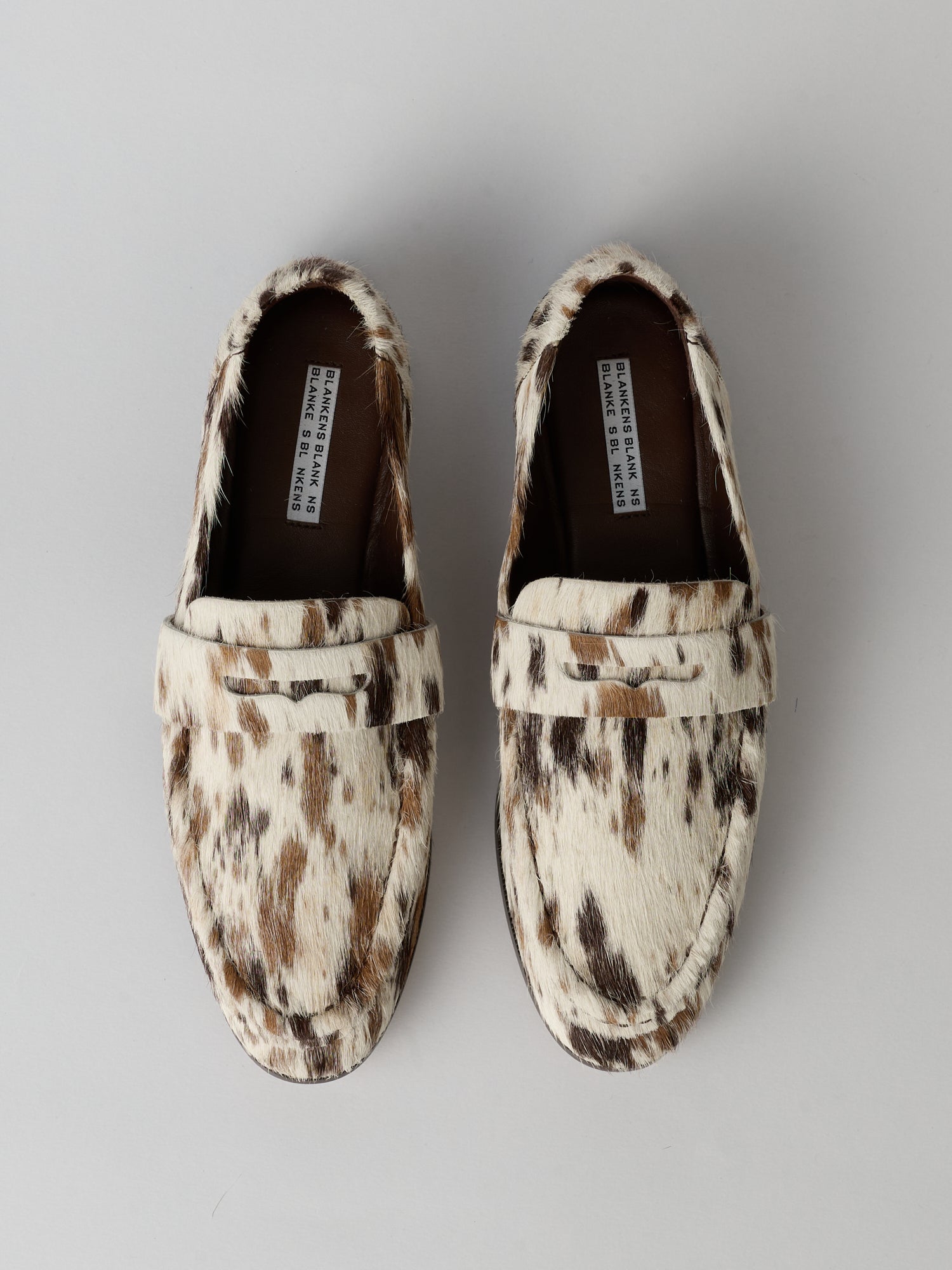 Pair of cow print loafers on a gray background