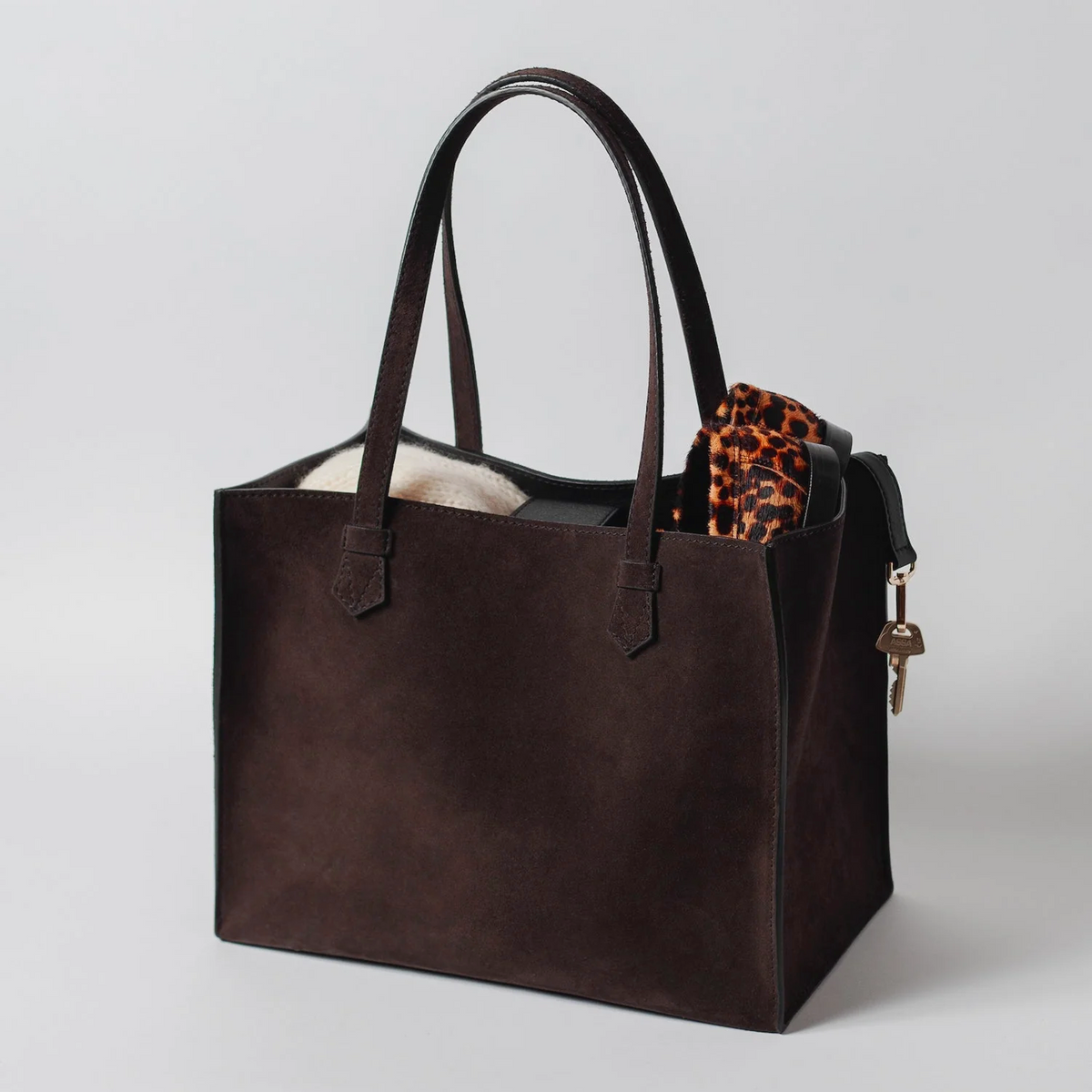 Brown suede tote bag with a leopard print item on a light gray background