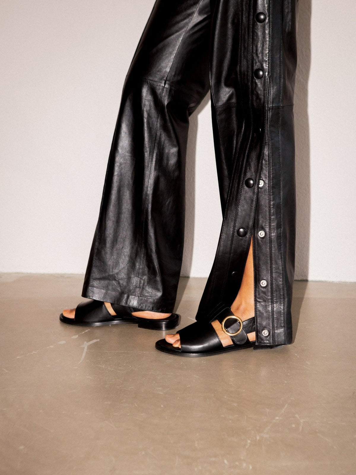 Person wearing black leather pants with a button detail on a neutral background