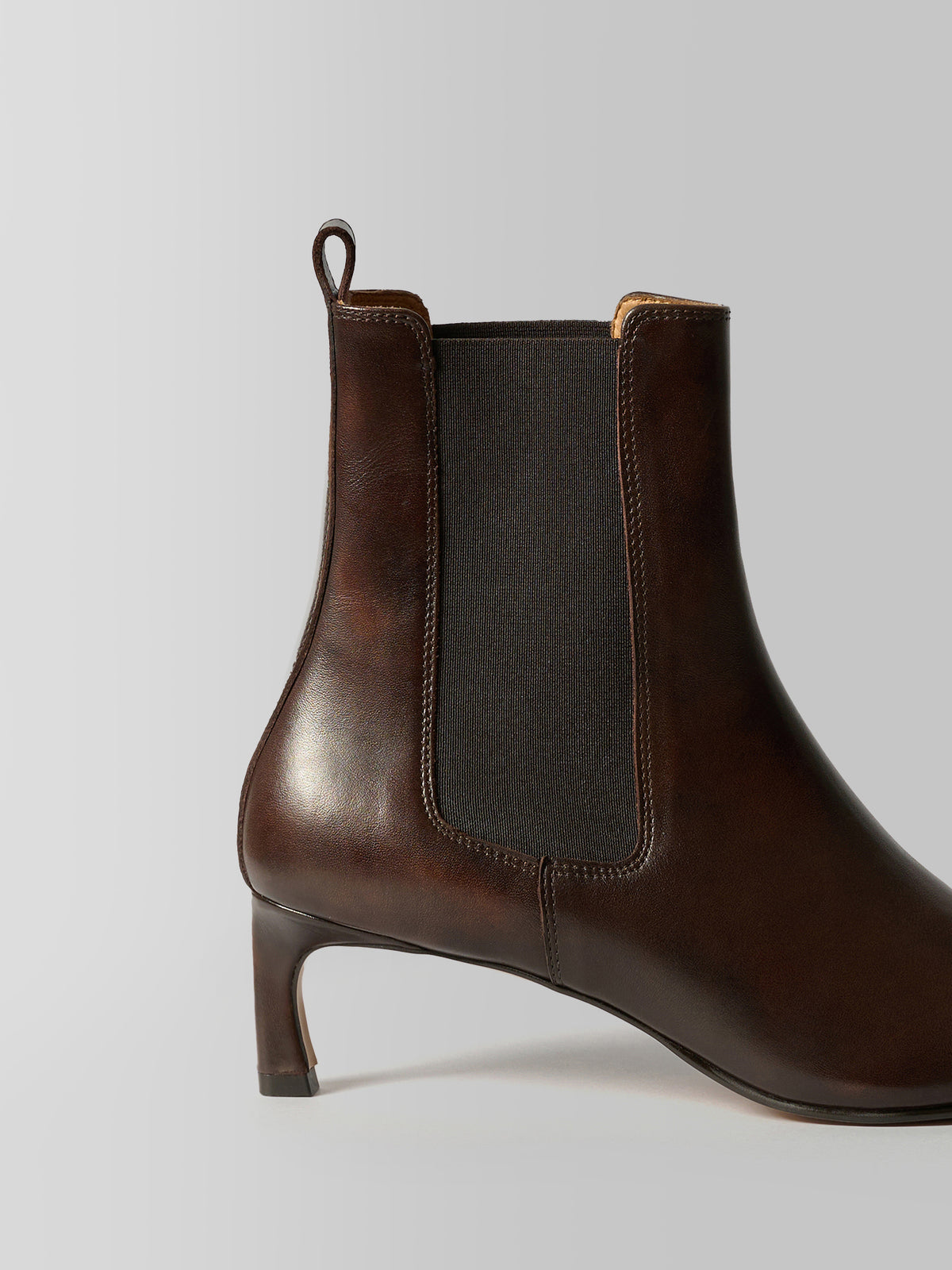 A dark brown leather ankle boot with a dark gray elastic side panel and a low block heel, shown from a side profile on a light gray background.