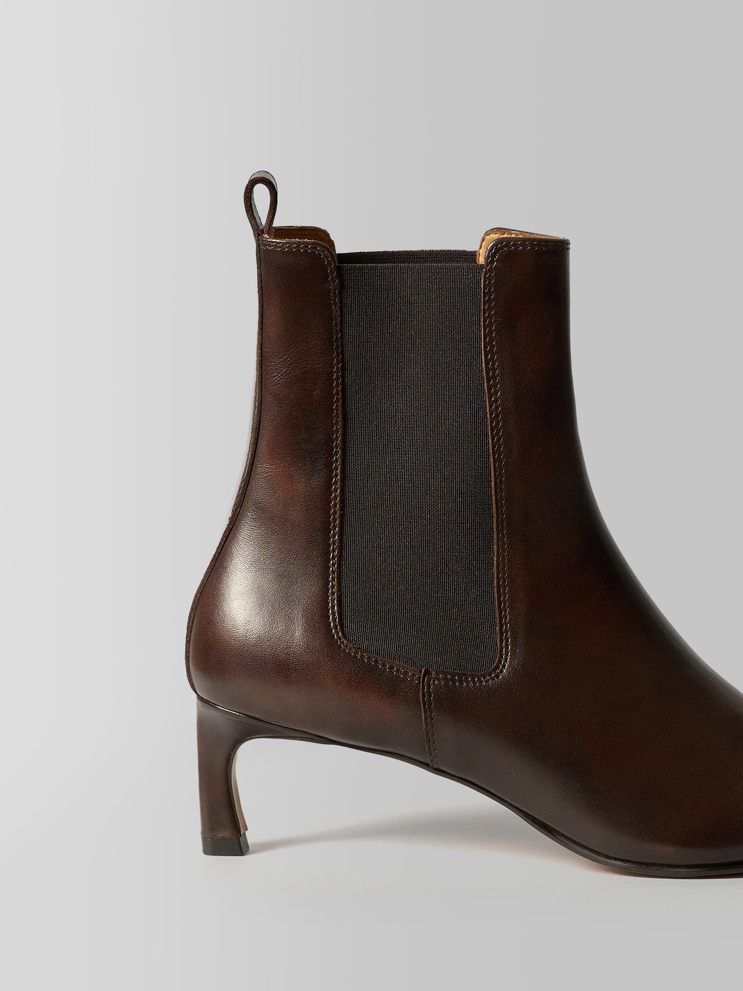 A dark brown leather ankle boot with a dark gray elastic side panel and a low block heel, shown from a side profile on a light gray background.