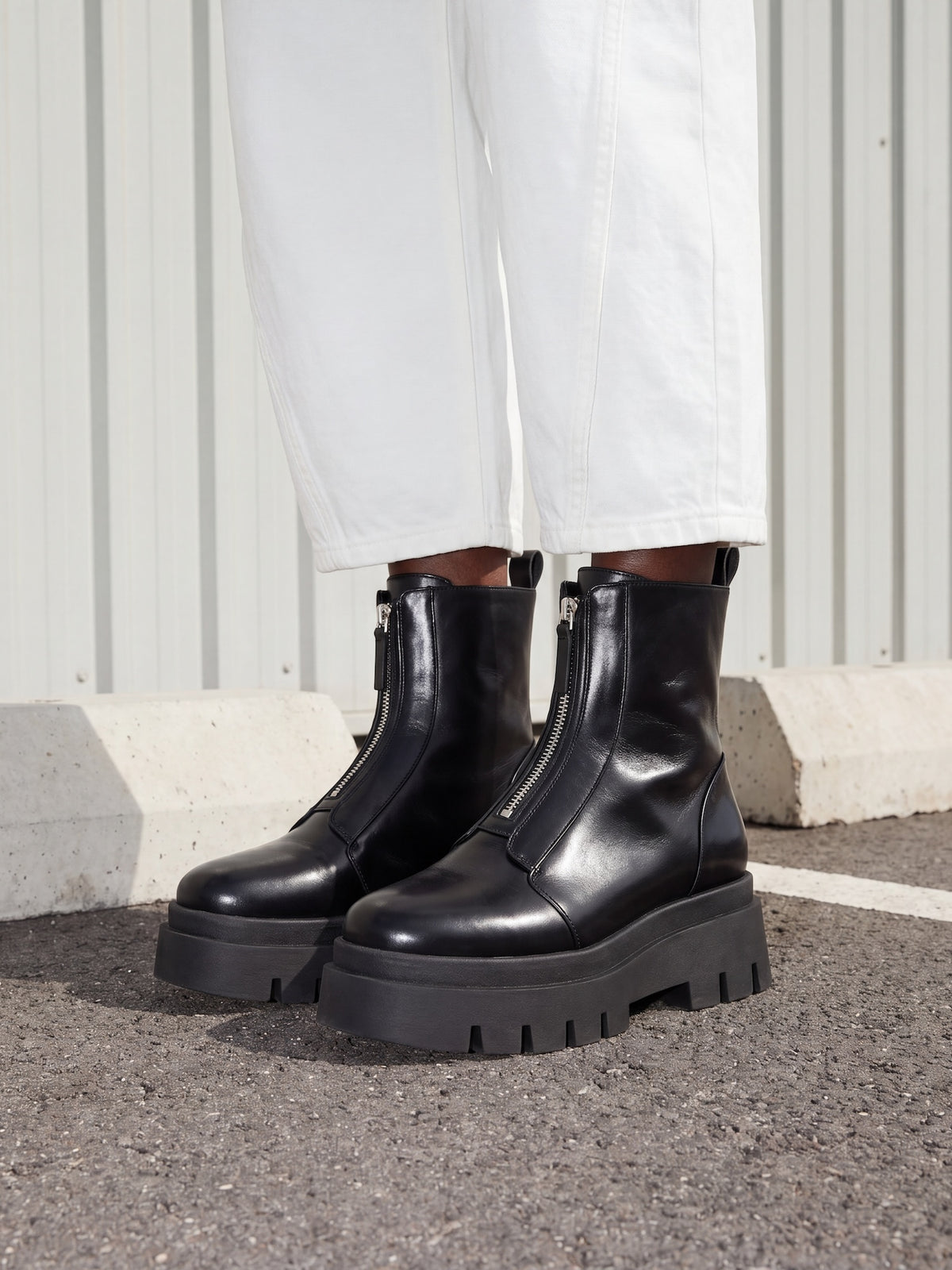 Black platform boots worn with white pants against a neutral background