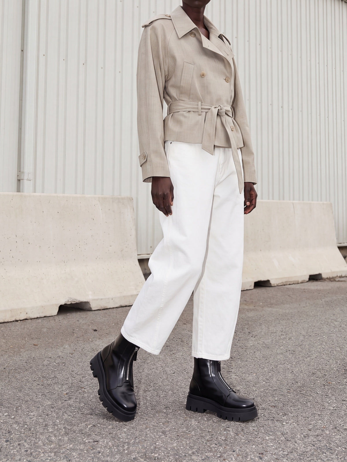 Person wearing a beige trench coat, white pants, and black boots on a neutral background