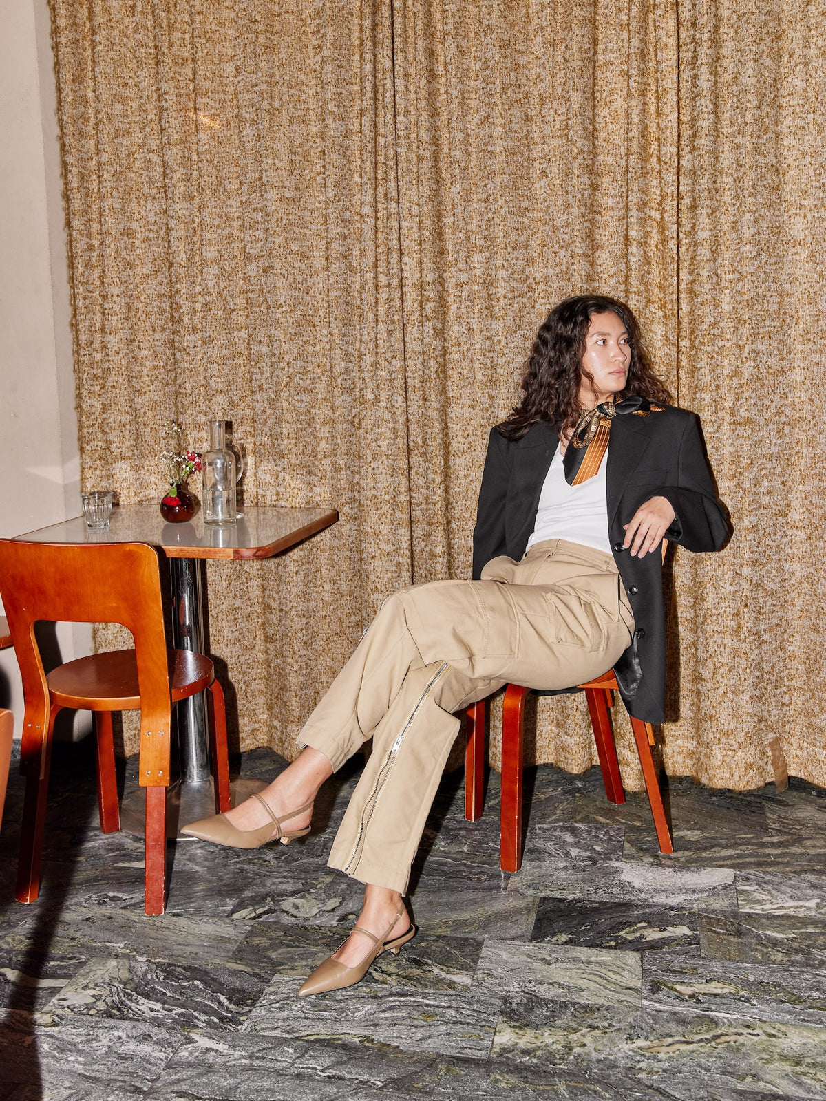 Woman sitting at a table in a room with a textured wall and wooden chairs.